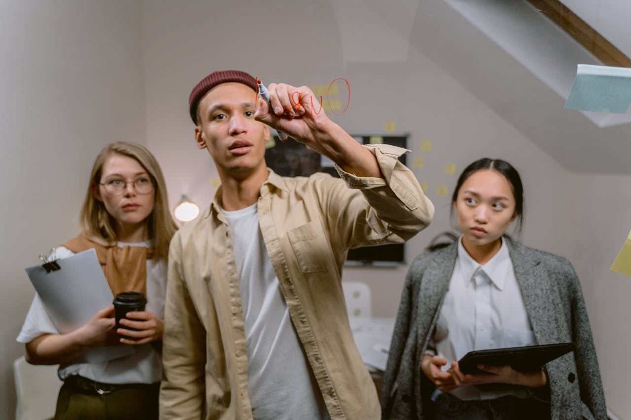 Three diverse young professionals brainstorming ideas on glass board in modern office setting.