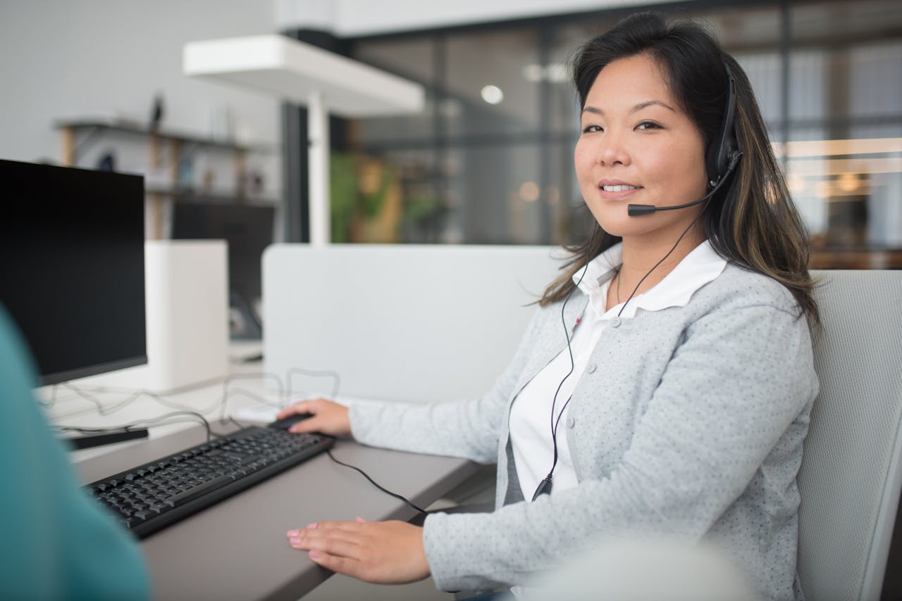 Asian woman wearing headset while working in a modern office and providing customer support.
